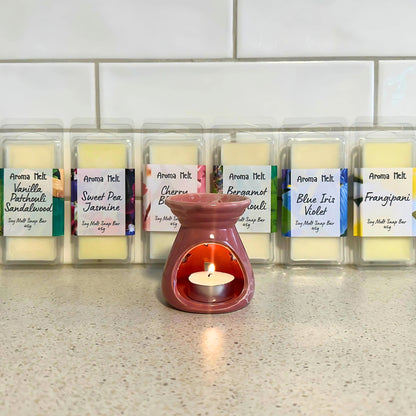  Wax warmer with a lit tealight candle melting six Aroma Melt soy wax melts in packaging, releasing fragrant aromas.